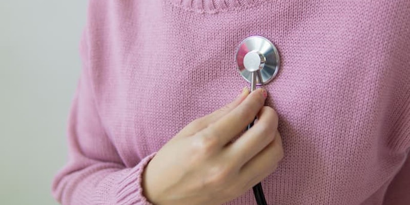 Pessoa com blusa rosa posicionando um estetoscópio sobre o peito para monitorar a saúde cardiovascular com hipertensão e doenças cardíacas tratadas com Selozok.