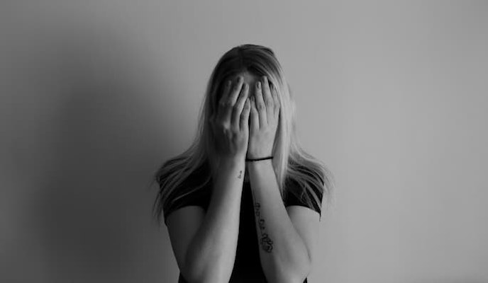 Mulher com as mãos cobrindo o rosto, em frente a uma parede lisa com ansiedade social tomando oxalato de escitalopram.