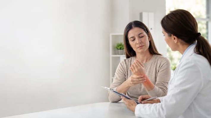 Mulher relatando dor e inflamação no punho durante consulta médica com condições inflamatórias e alérgicas que podem ser tratadas com a prednisolona.