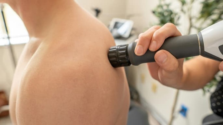 Pessoa recebendo aplicação de aparelho terapêutico na região do ombro com dor muscular.