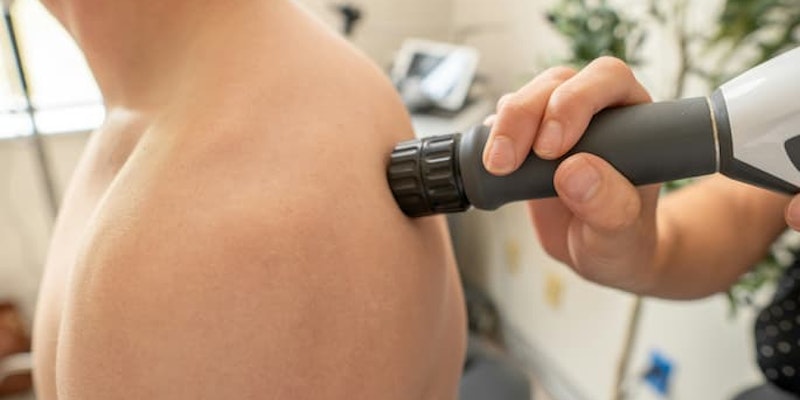Pessoa recebendo aplicação de aparelho terapêutico na região do ombro com dor muscular.