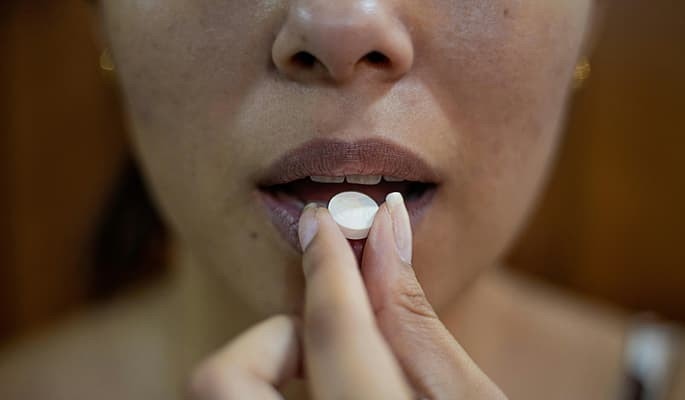 Pessoa levando um comprimido de doxiciclina à boca para ingestão.