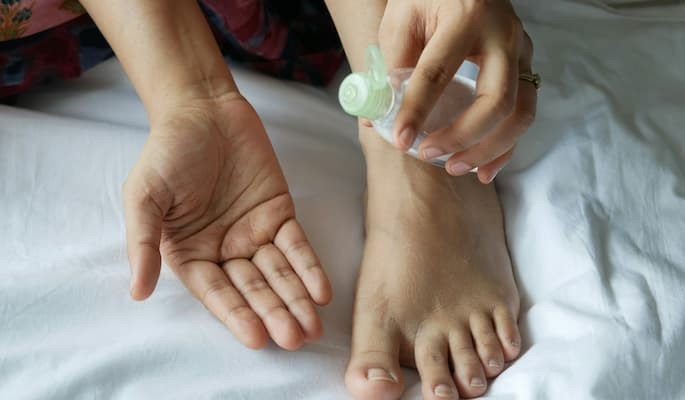 Pessoa aplicando um medicamento líquido na região do pé com a doença gota.