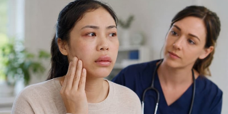 Paciente tocando o rosto com aparente inchaço na região dos lábios e da face durante consulta médica com angioedema alérgico.
