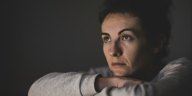 Pessoa sentada com os braços apoiados nos joelhos e olhar distante com sofrimento emocional associados ao transtorno obsessivo-compulsivo (TOC).