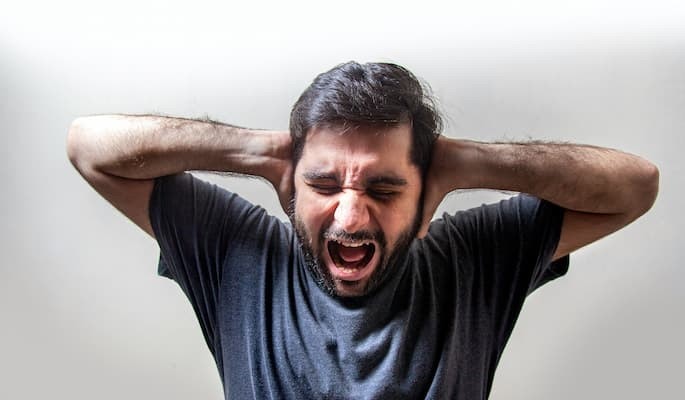 Homem com as mãos cobrindo os ouvidos, olhos fechados e expressão de intenso sofrimento com crise de transtorno do pânico.
