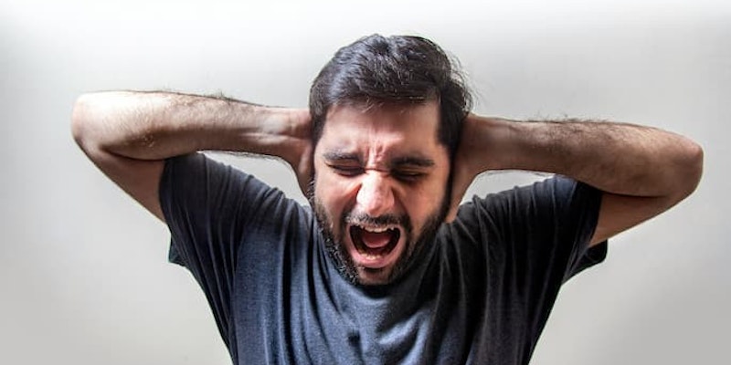 Homem com as mãos cobrindo os ouvidos, olhos fechados e expressão de intenso sofrimento com crise de transtorno do pânico.