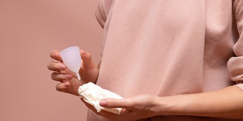 Pessoa segurando um coletor menstrual e um absorvente descartável como opções de higiene durante o período menstrual.