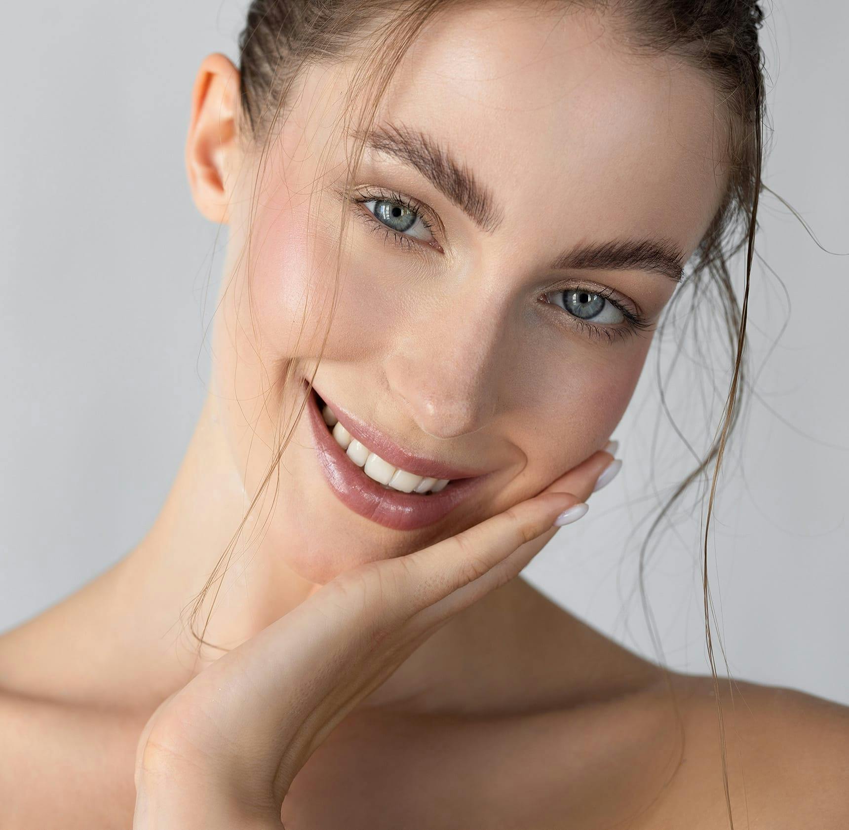woman touching her cheek, smiling and tilting her head