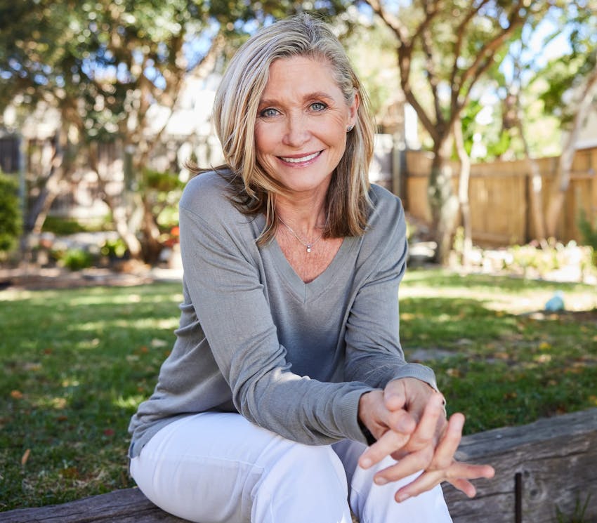 woman sitting outdoors smiling with her hands together