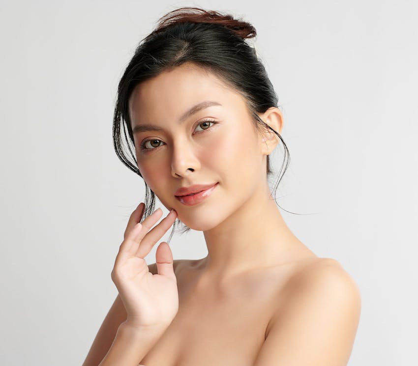 asian woman with her hair tied up smiling with her hand near her cheek