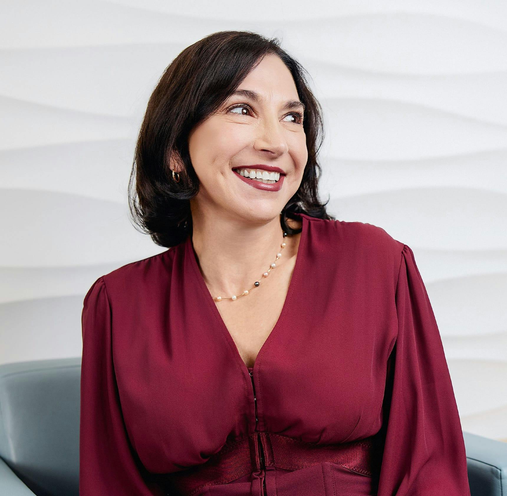 female patient in maroon dress sitting down and smiling