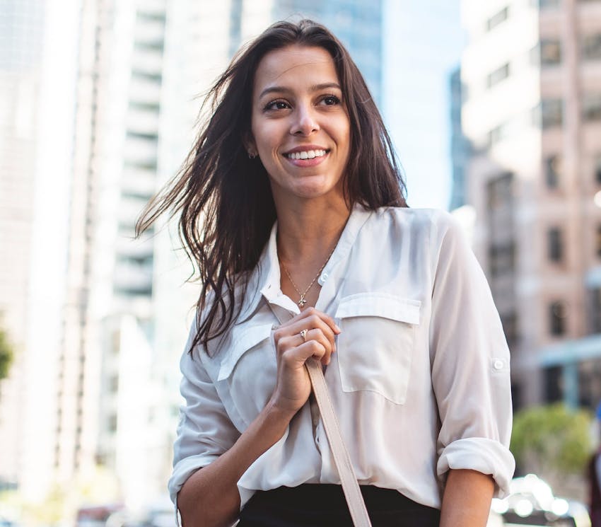 woman out in the city smiling and holding her purse strap