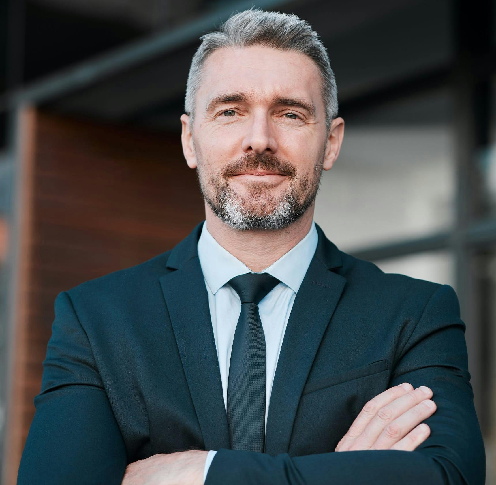 man crossing his arms and wearing a black suit
