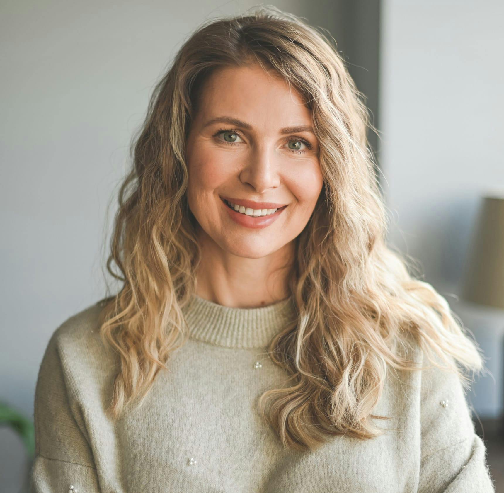 woman with blonde curly hair wearing a beige sweater