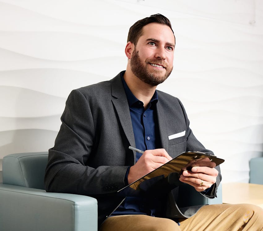 man sitting in couch filling out paperwork on clipboard