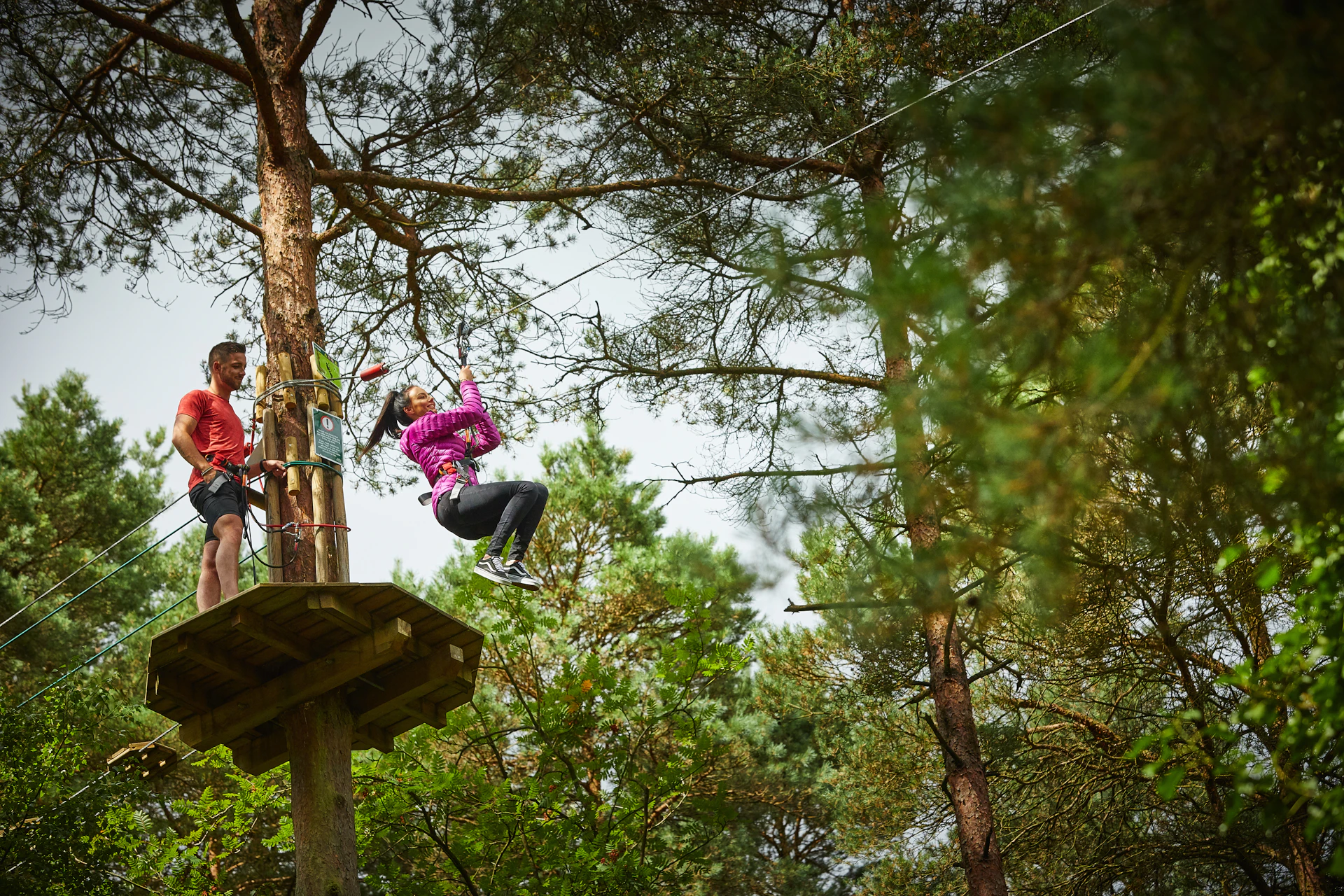 A person on a zip wire while another person watches from a platform.