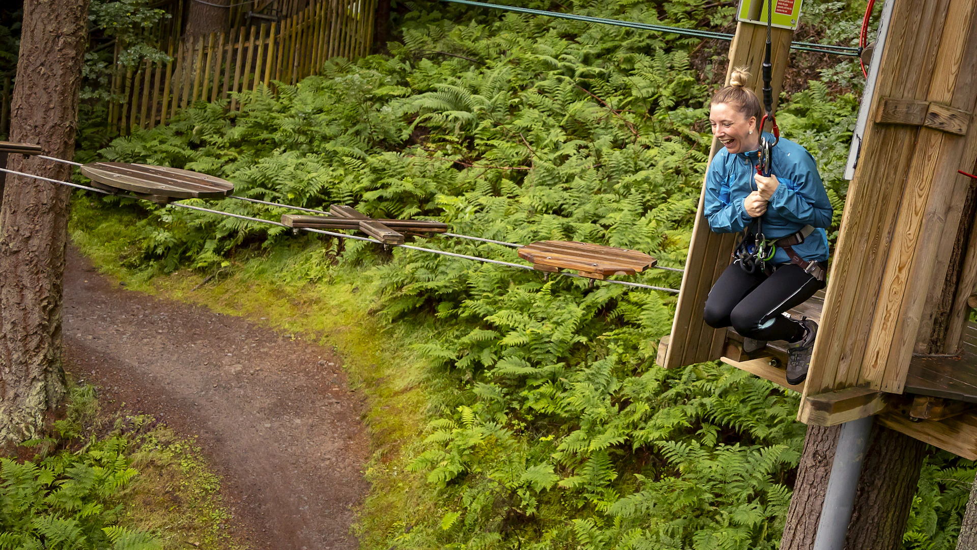 A person grinning as they get ready to swing from a high ropes course.