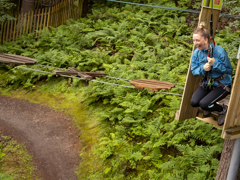 A person grinning as they get ready to swing from a high ropes course.