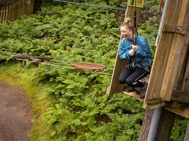 A person grinning as they get ready to swing from a high ropes course.
