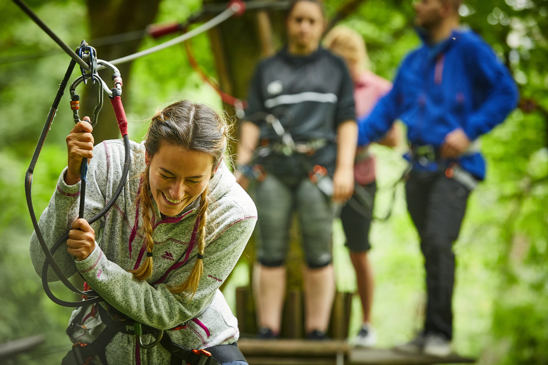 A person crossing a high ropes course while three people watch from a platform.