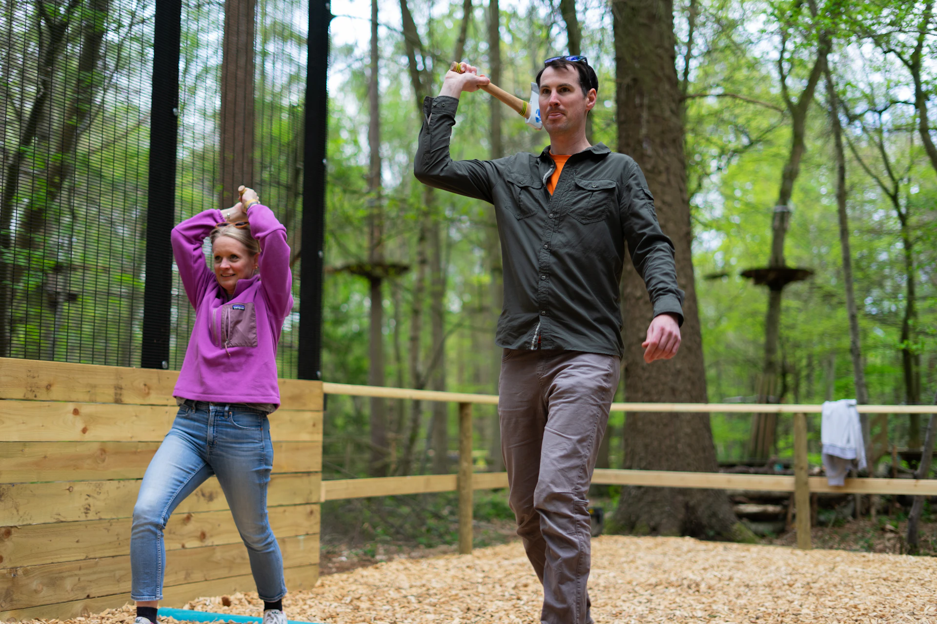 A man and a woman launch axes at a target in the forest on a fun day out
