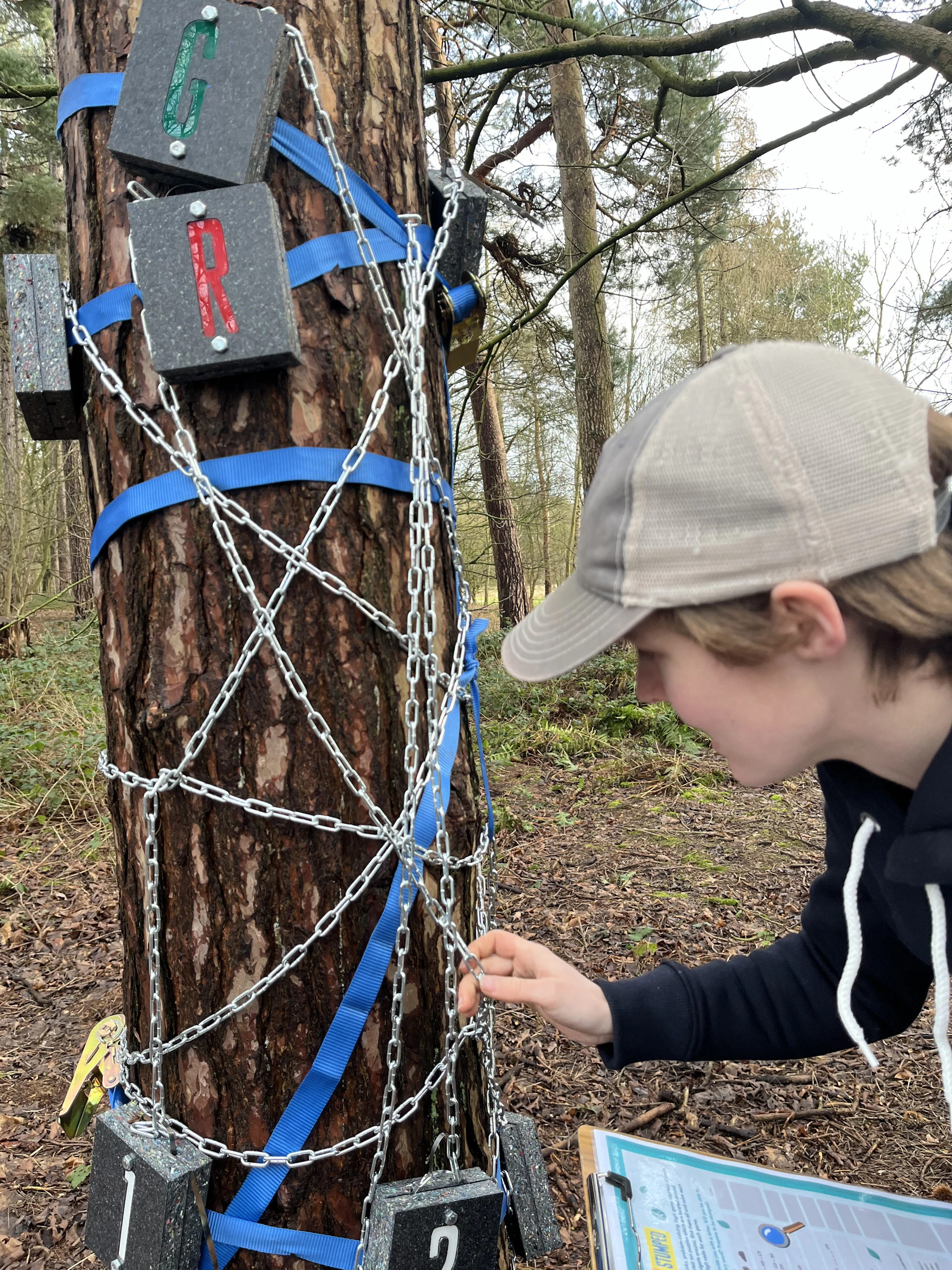A boy attemps a puzzle on Go Ape's Stumped featuring chains wrapped around a  tree