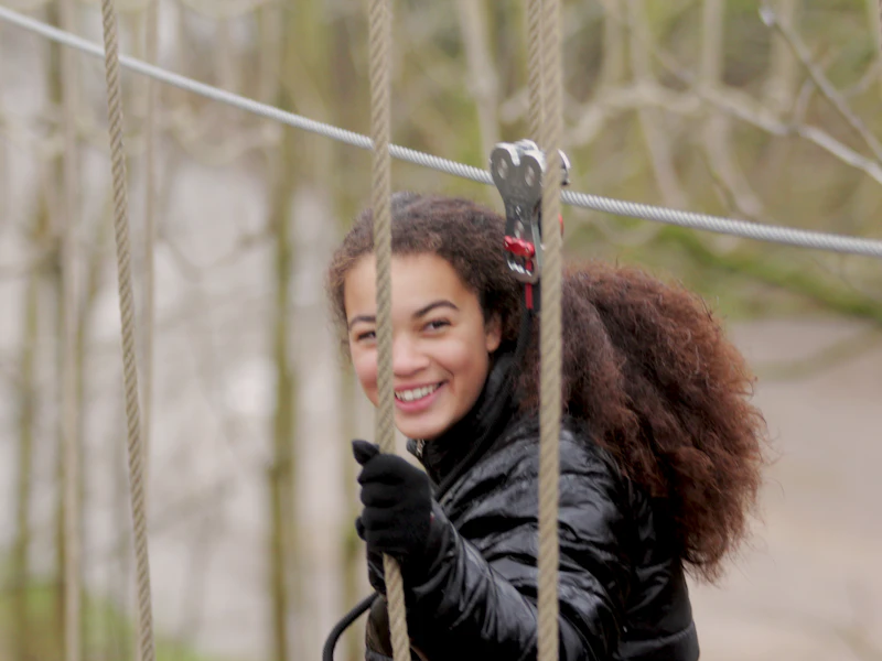 Young person smiles while crossing a high ropes course.