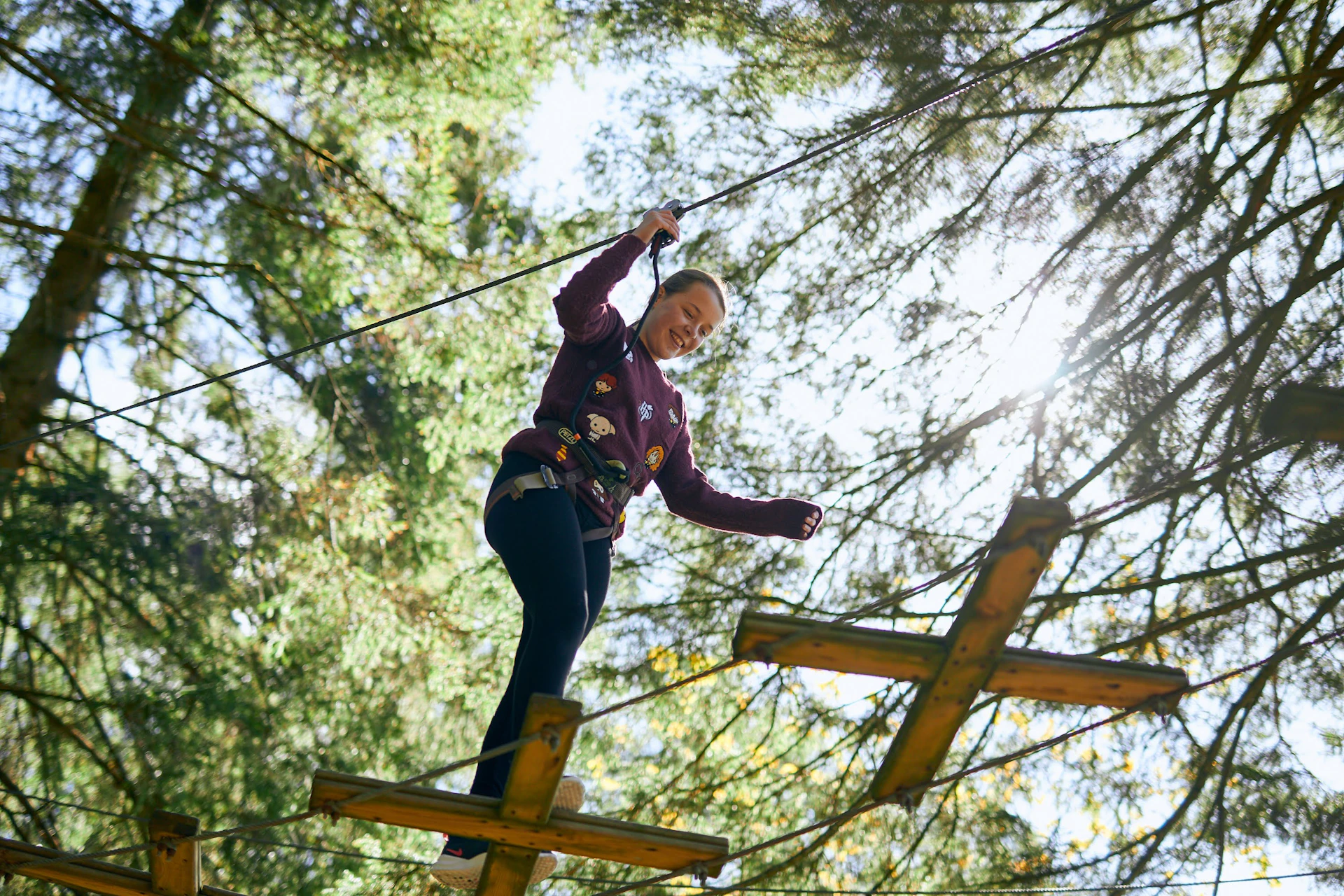 Young person smiles while crossing a high ropes course.