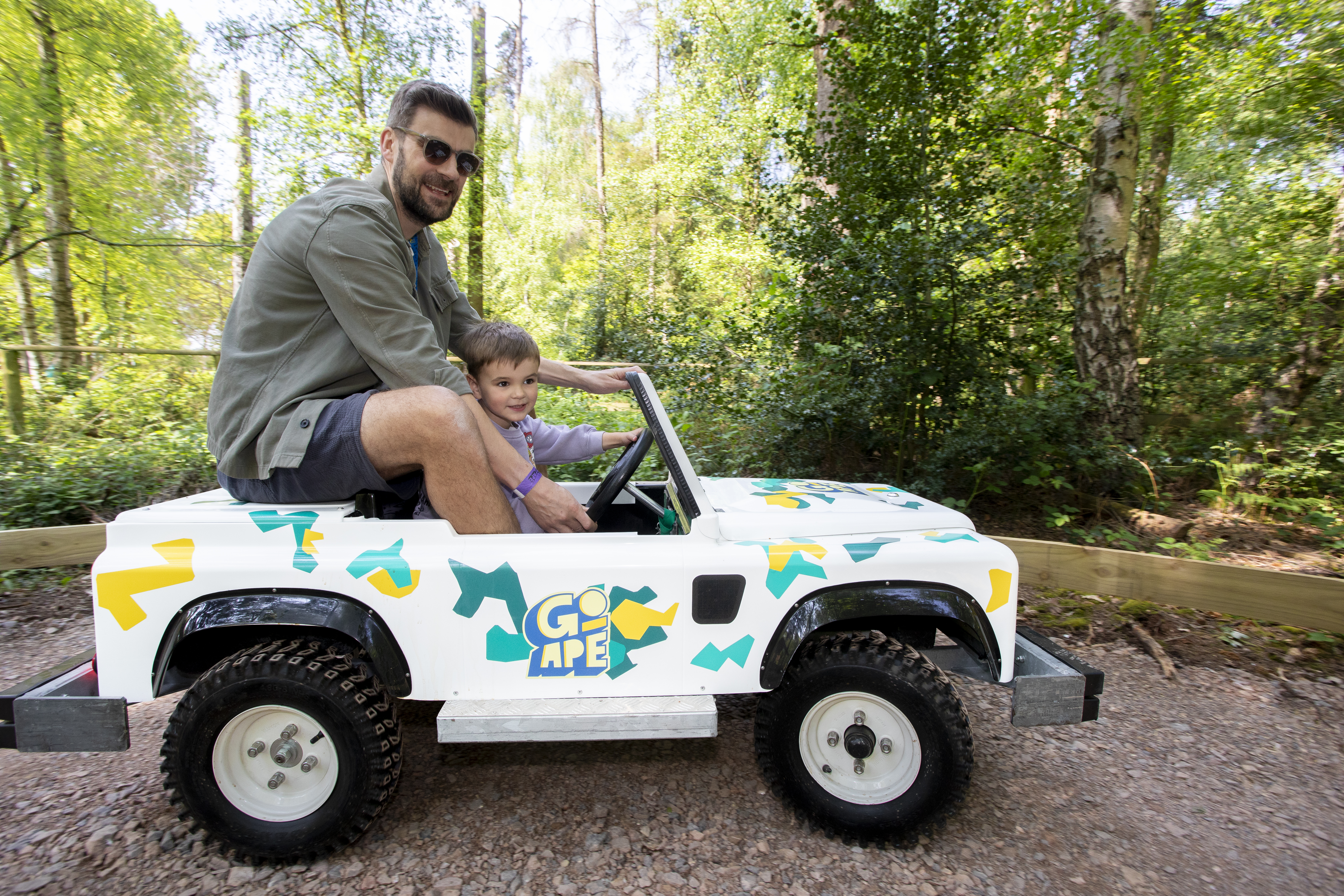 Adult and young person in a Mini Land Rover on a track in the forest.