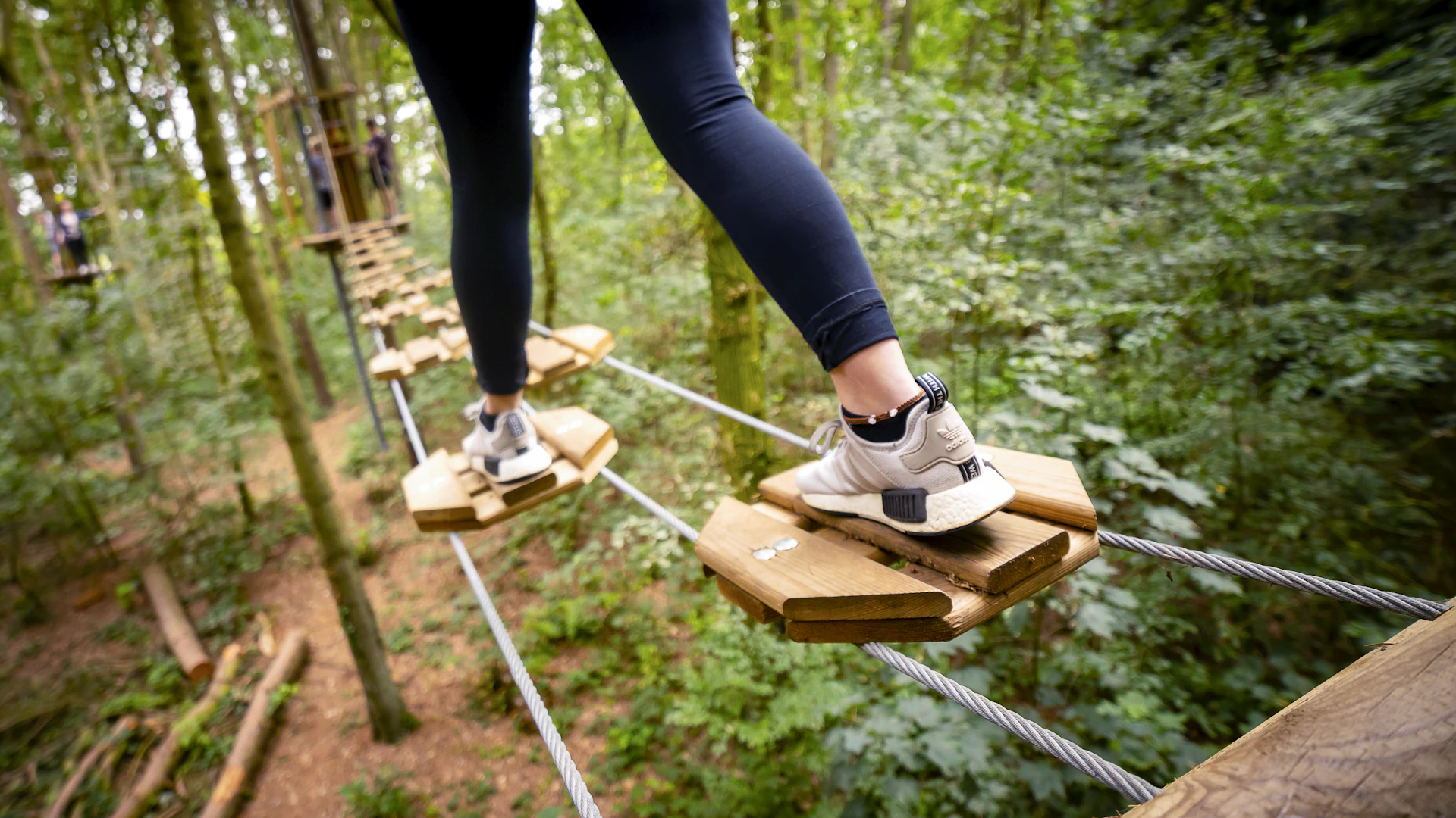 Focus on a person's trainers as they step across a high ropes crossing.