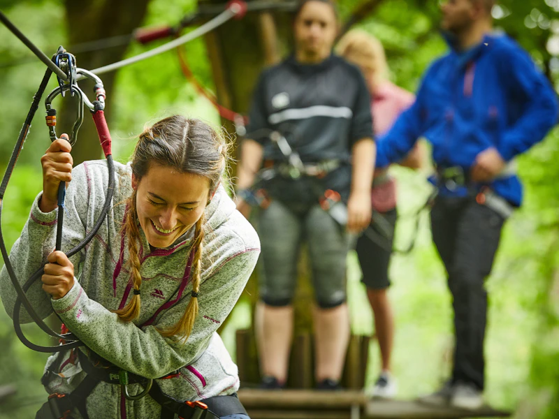 High ropes crossing fun A woman laughs on a Go Ape crossing whilst her freinds watch on from a treetop platform behind her