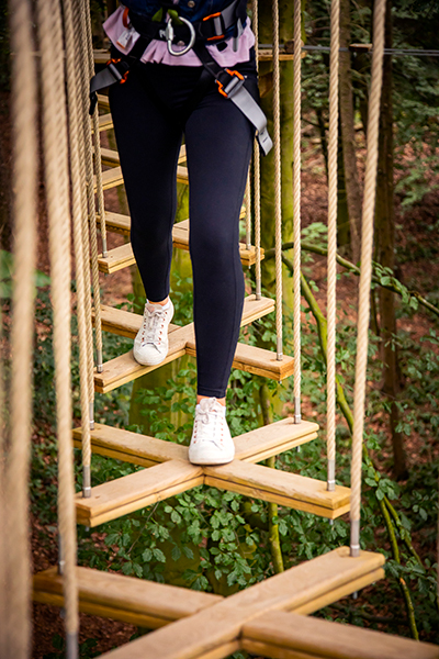 Focus on a person's trainers as they step across a high ropes crossing.