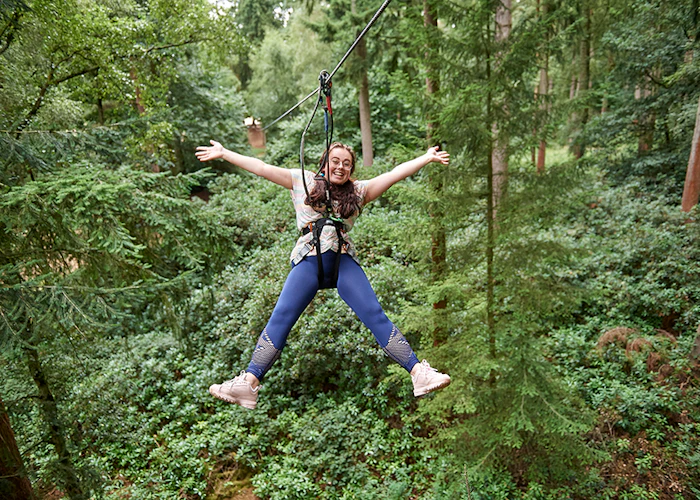 Person on a zipline with their arms wide in a forest.