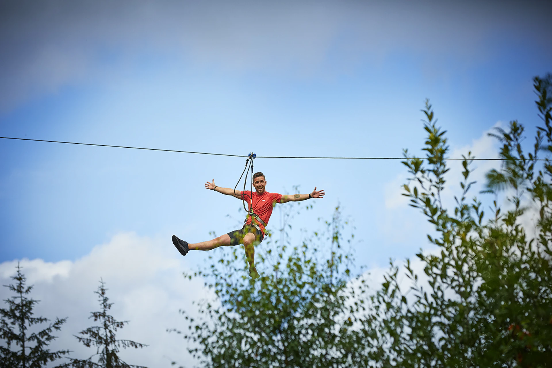 Person on a zipline with their arms wide on a sunny day.