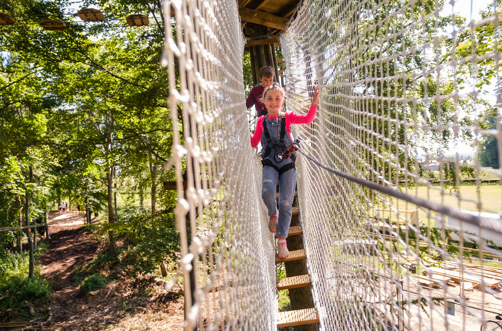 Young person smiles while crossing a high ropes course.