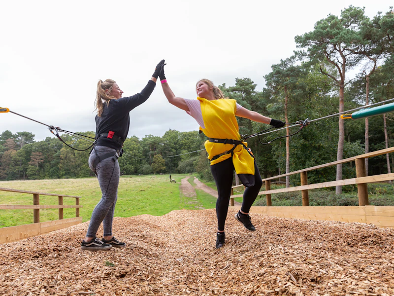 A bride to be and her freind celebrate with a high-five on a Go Ape zip wire landing site