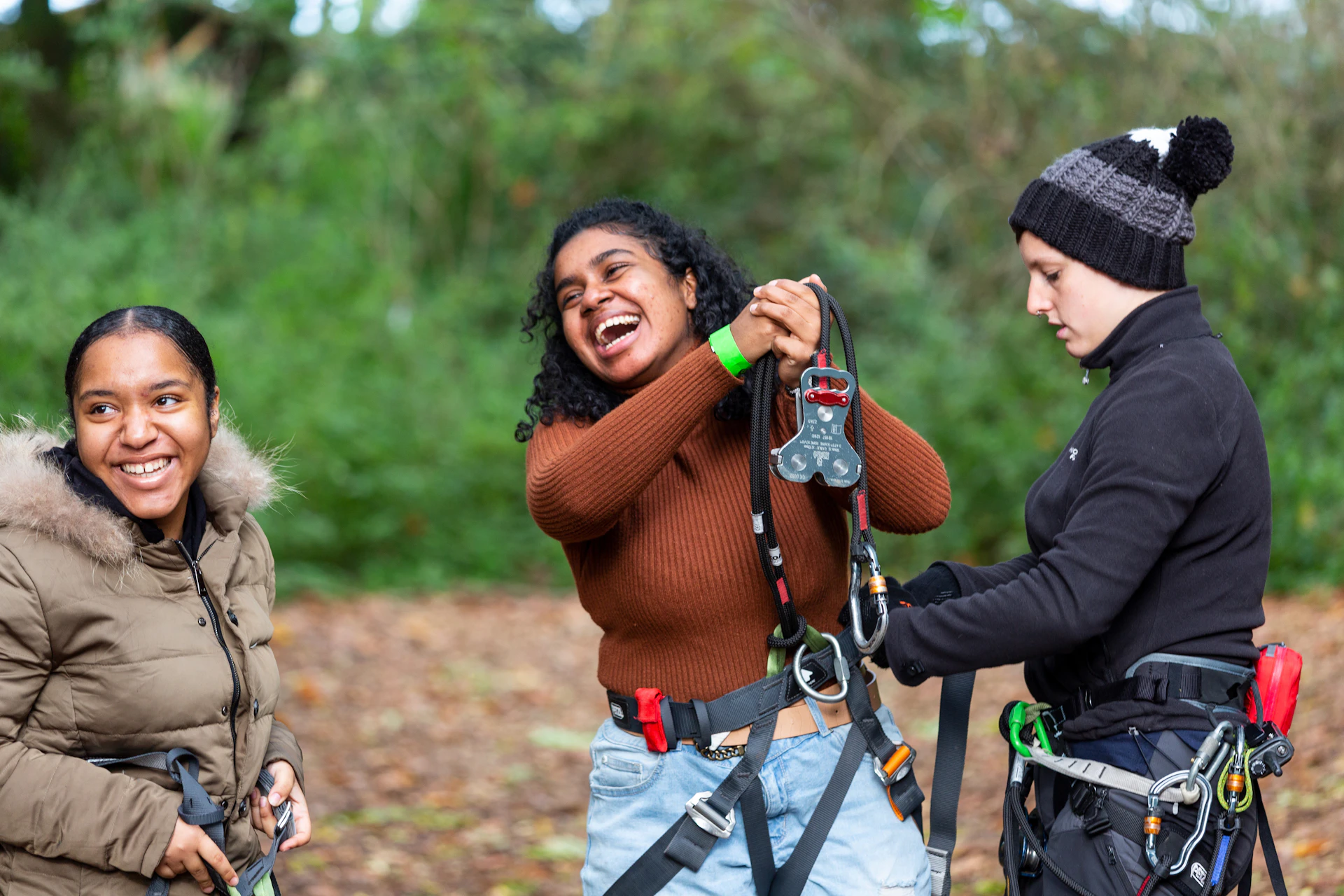 Two people laughing while an instructor helps with their harnesses.