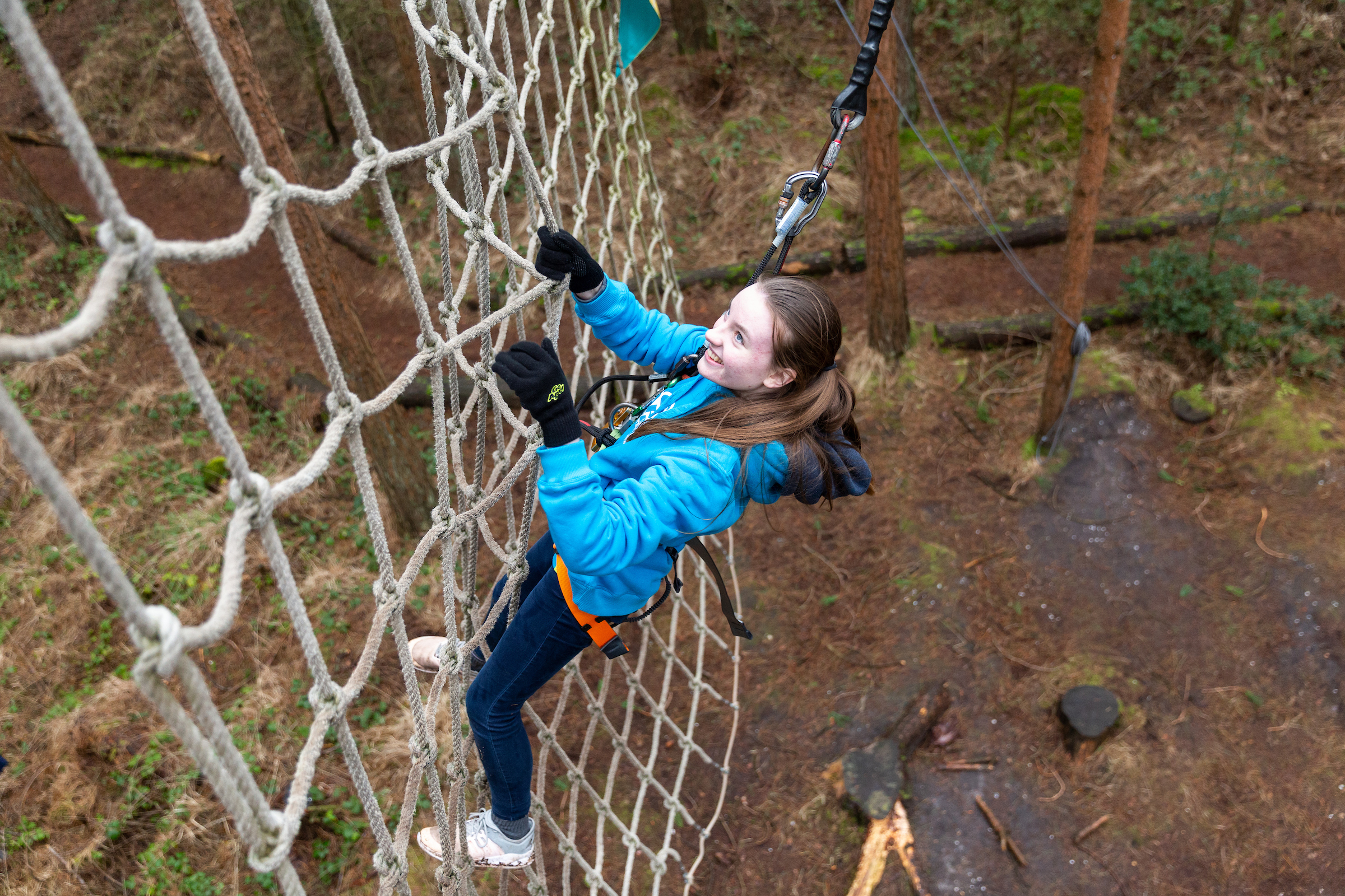 A girl smiles as she scales a cargo net in the forest
