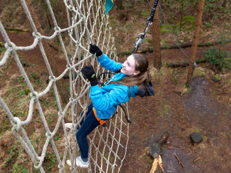 A girl smiles as she scales a cargo net in the forest