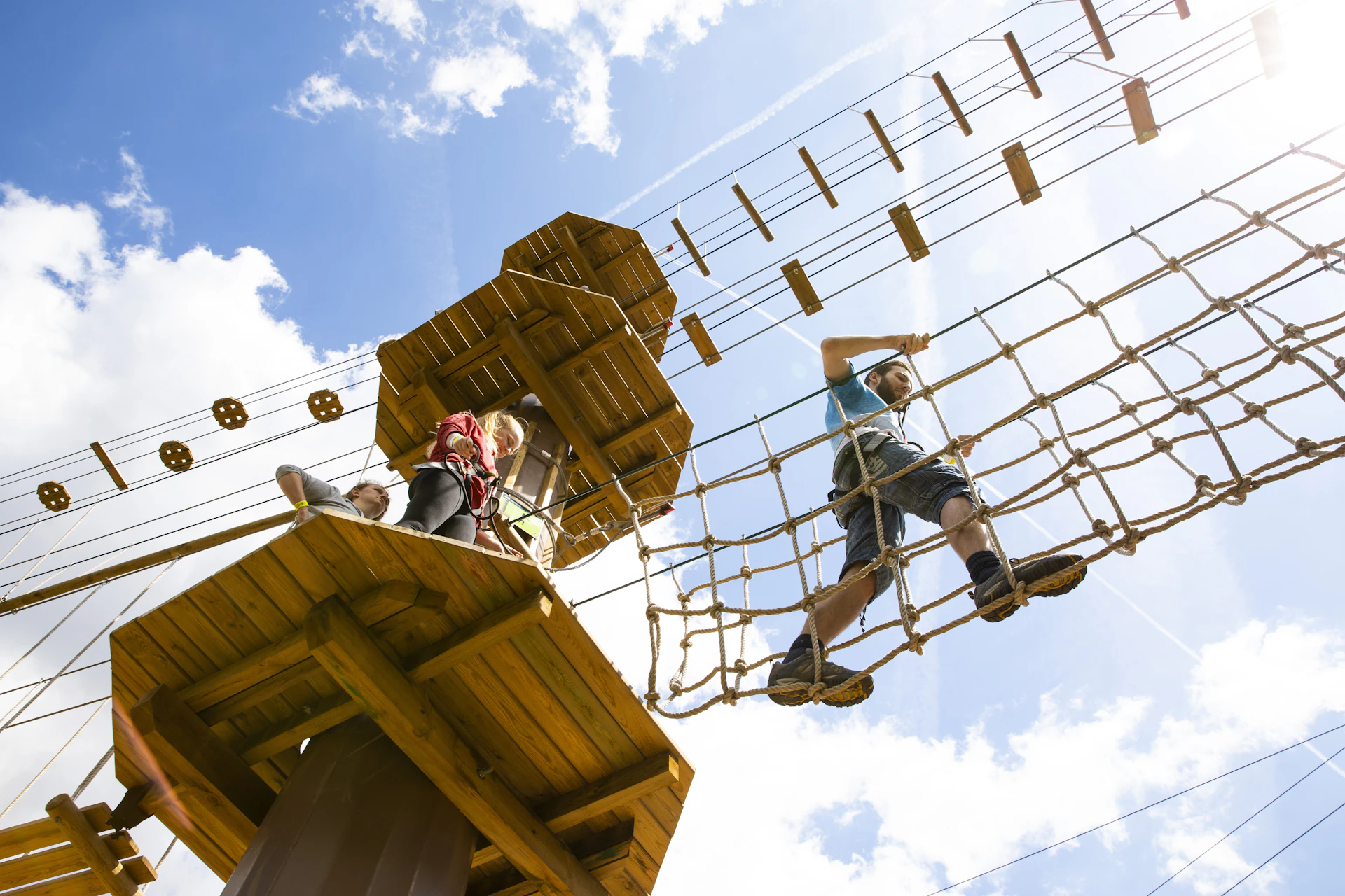 Person high above crosses a rope bridge on a sunny day.