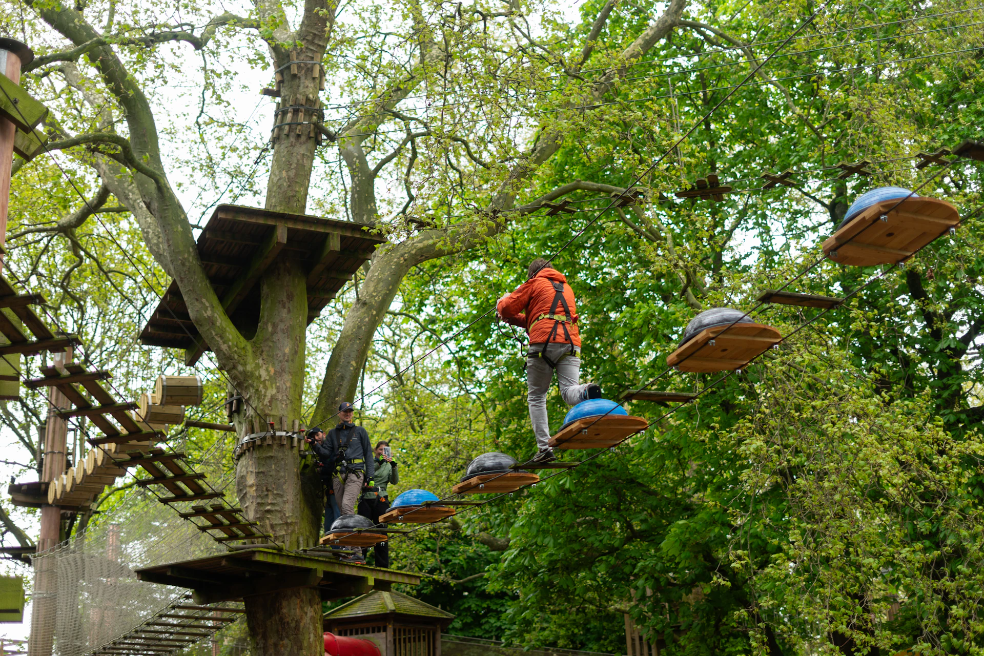 Person crossing a high ropes course while another waits on the platform.