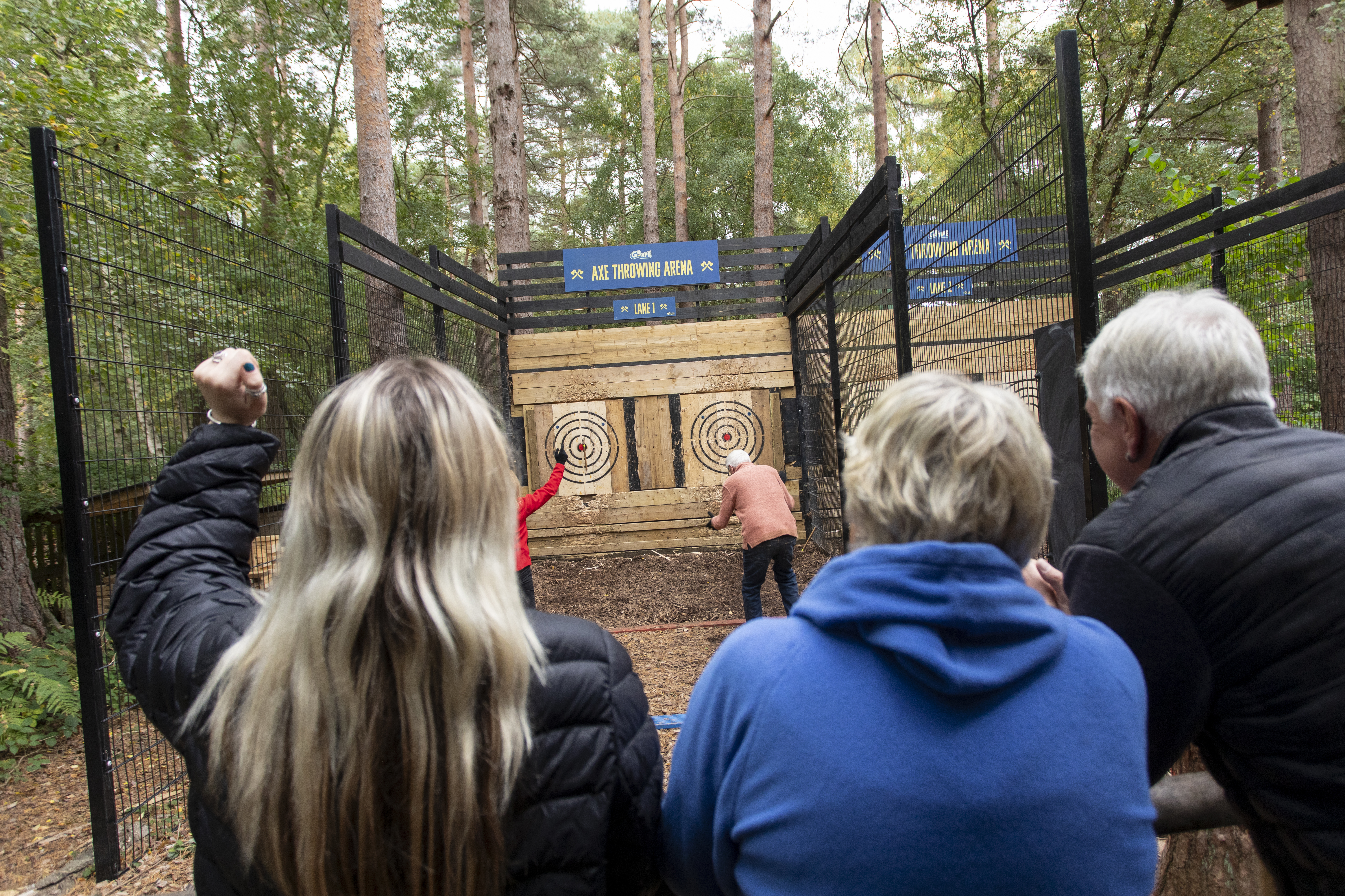 A group watches and cheers as two people through axes at targets.