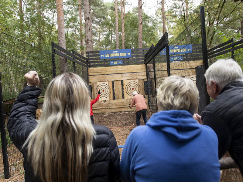 A group watches and cheers as two people through axes at targets.