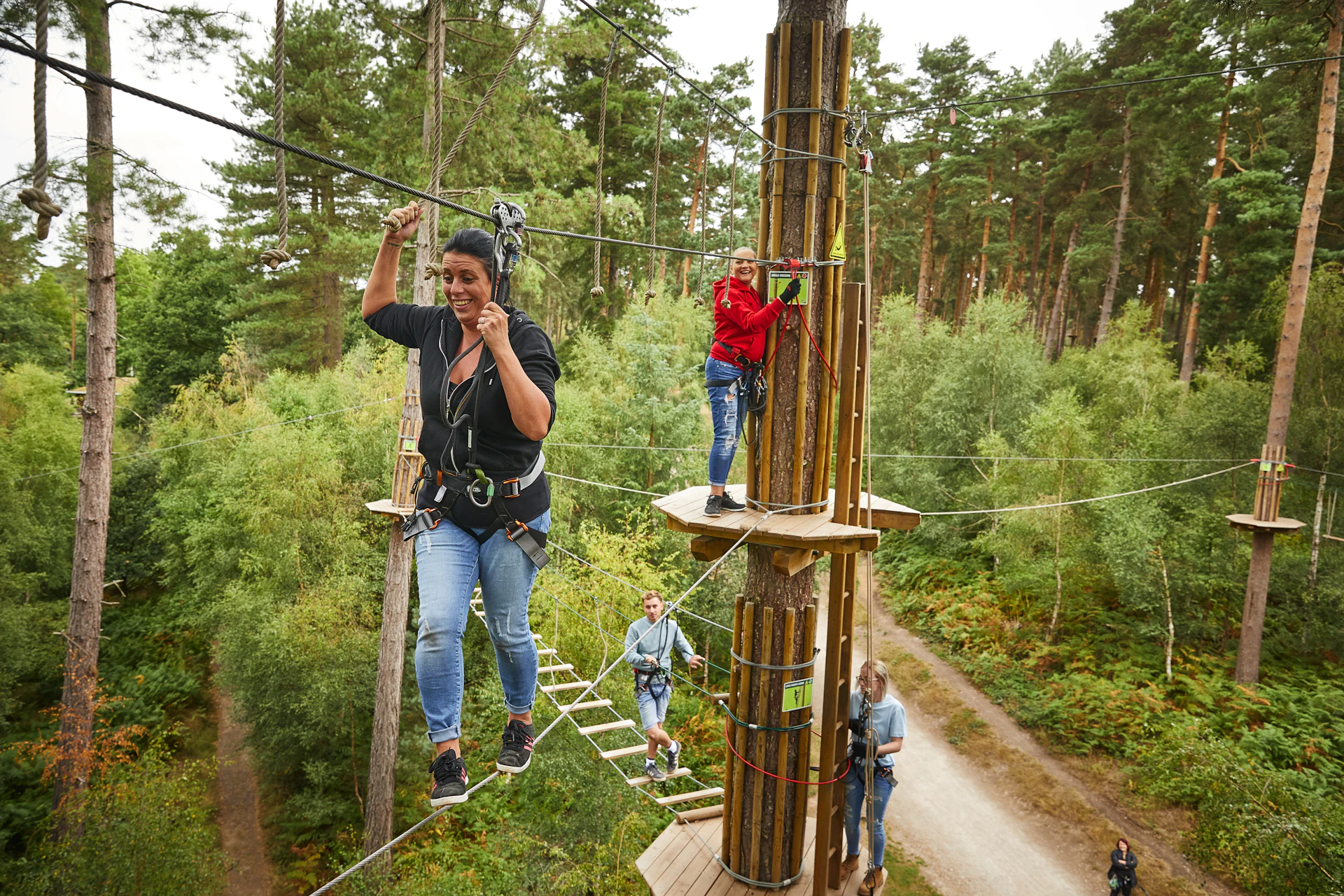 Person on a high ropes crossing while another waits on a platform.