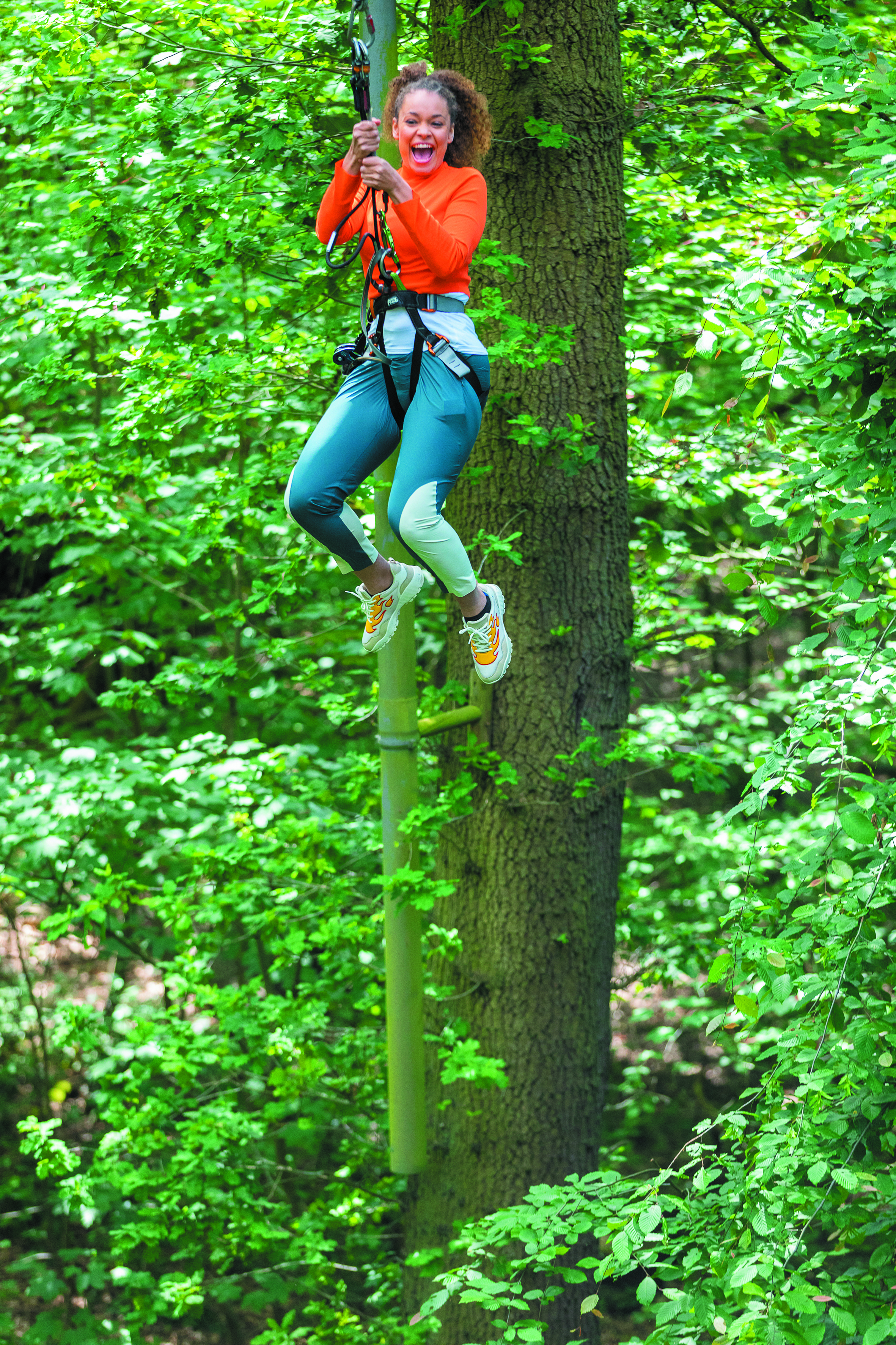 Person on a swing on a high ropes course wearing a harness while grinning.