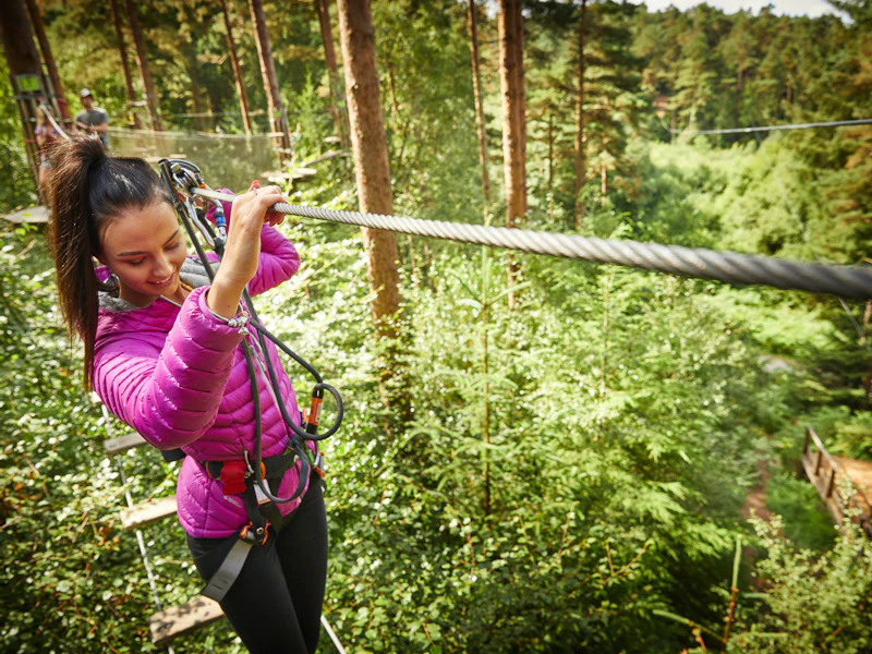 A woman wearing a pink jacket balnces on a Go Ape high ropes crossing