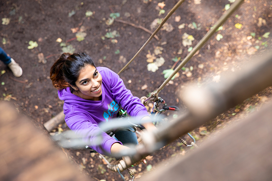 Person climbs a ladder on a high ropes course while smiling.