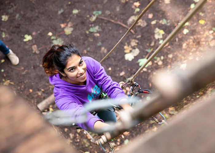 Person climbs a ladder on a high ropes course while smiling.