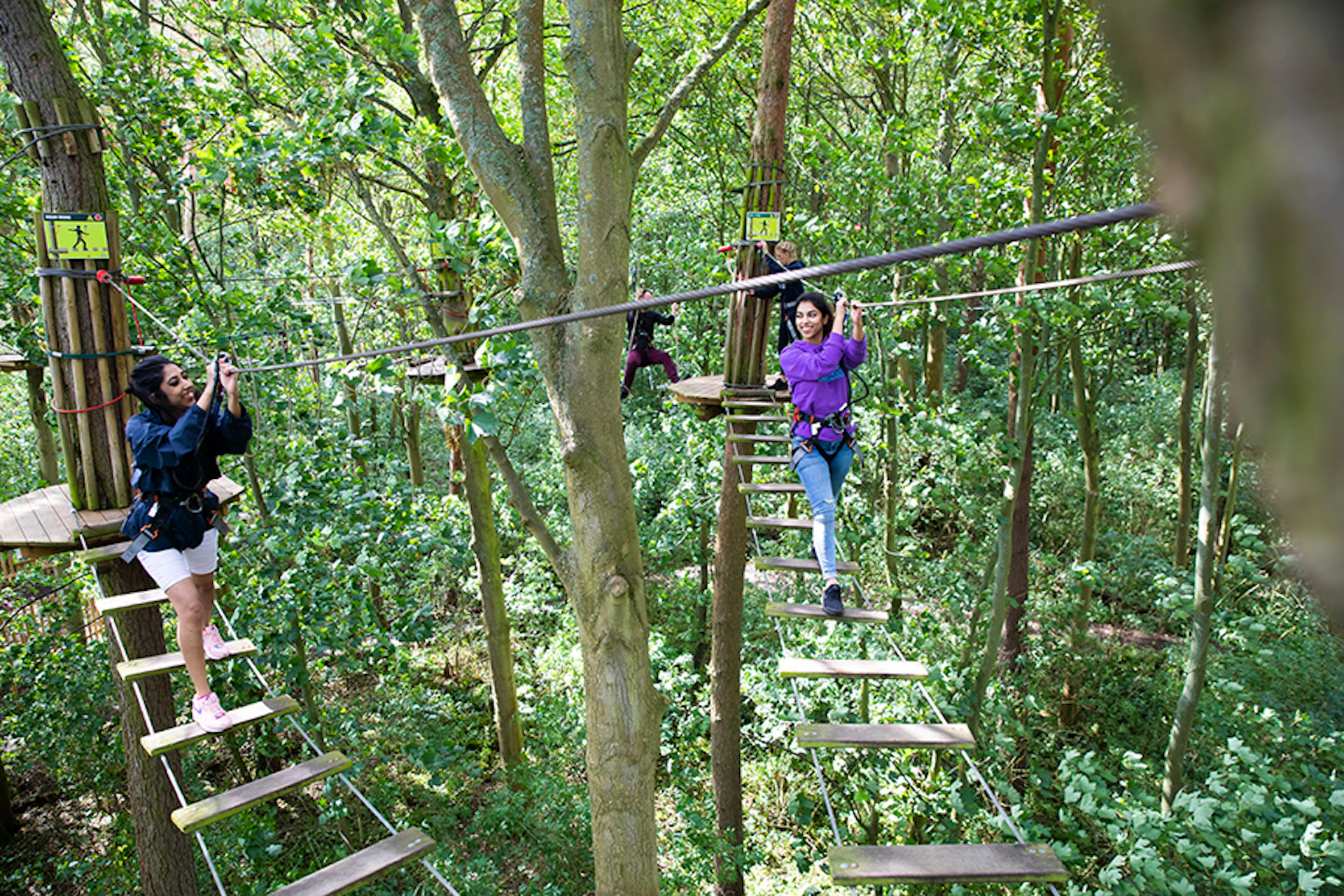 Two people on two high ropes crossings.